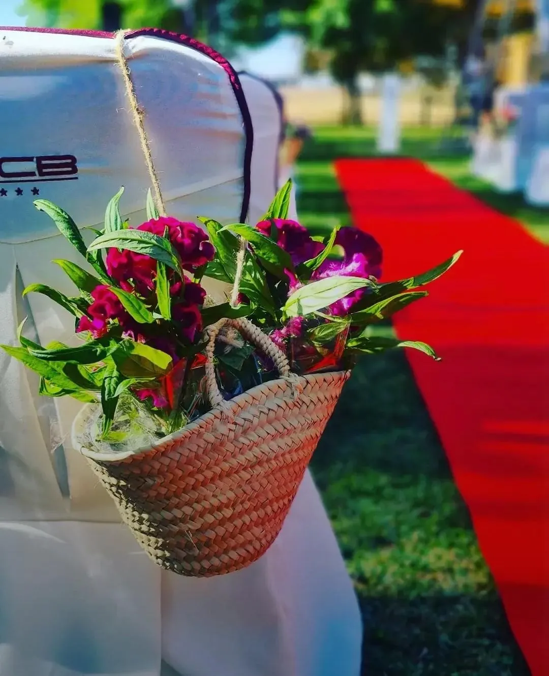 Cesta con flores fucsia colgada en silla de boda con alfombra roja